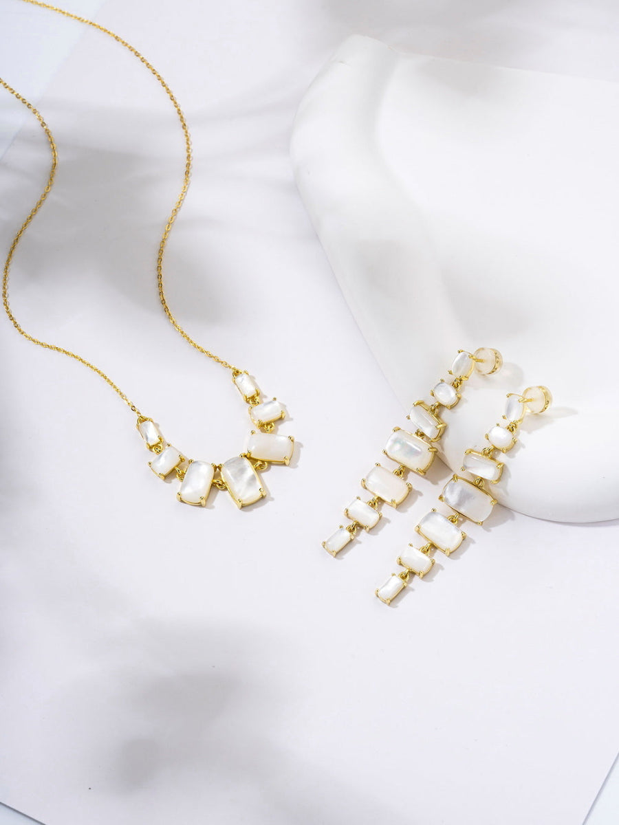 These elegant graduated dangle earrings and necklaces feature white Mother of Pearl stones and sparkling 5A cubic zirconia, set in 14K gold-plated 925 sterling silver. Crafted by Joy & Rachel, they showcase timeless beauty and exceptional craftsmanship.