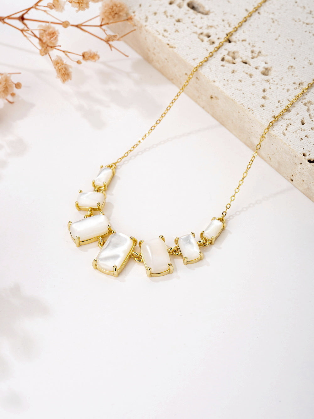This elegant graduated necklace features radiant white Mother of Pearl stones complemented by sparkling 5A cubic zirconia accents. The chain is crafted from 925 sterling silver and finished with 14K gold plating for a luxurious touch. The adjustable chain measures 16 inches, with an additional 2-inch extension to accommodate 17- or 18-inch lengths. Designed with a secure lobster clasp, this necklace measures 0.5 inches in pendant width and is a part of Joy & Rachel's refined collection.